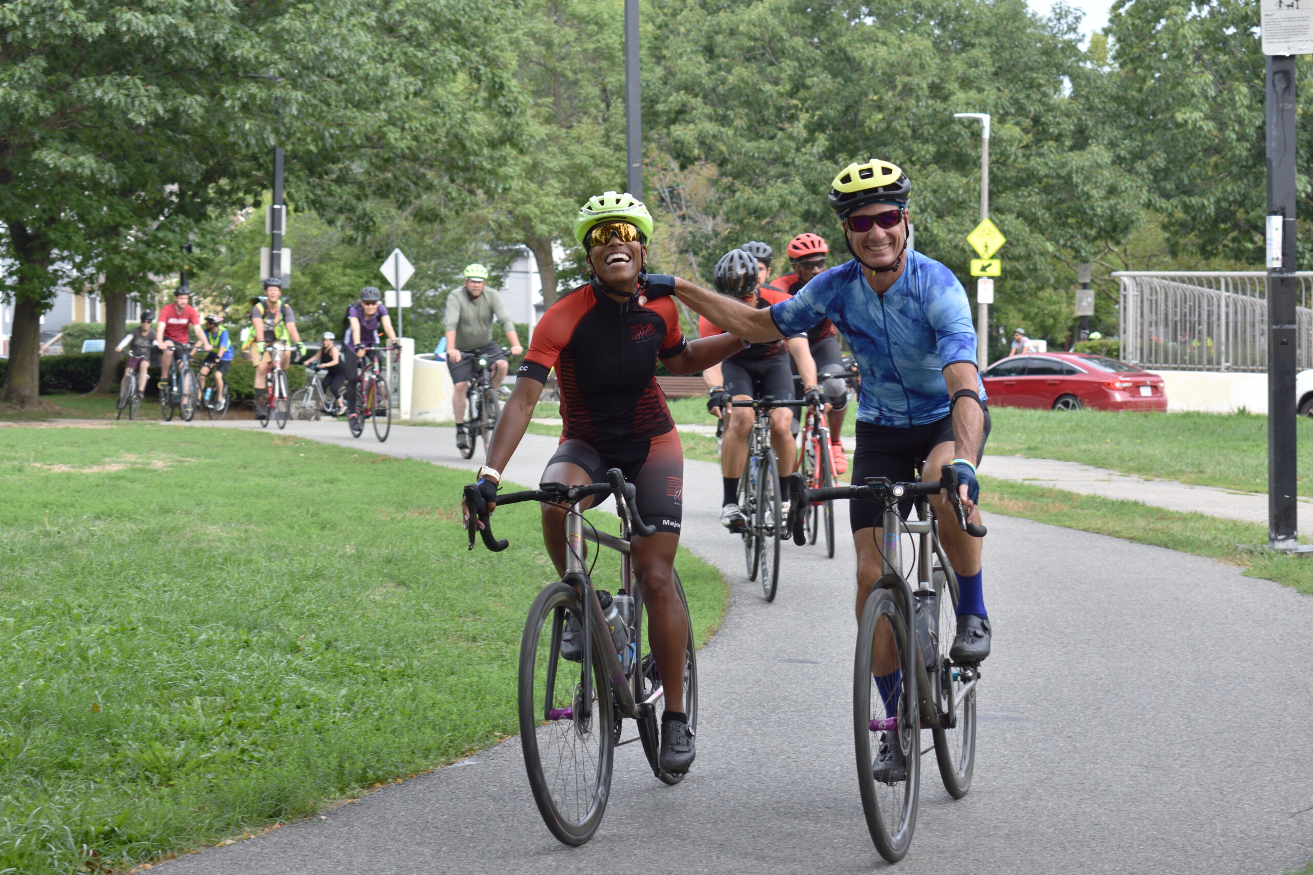 Two cyclists link hands while riding their bikes and smiling.
